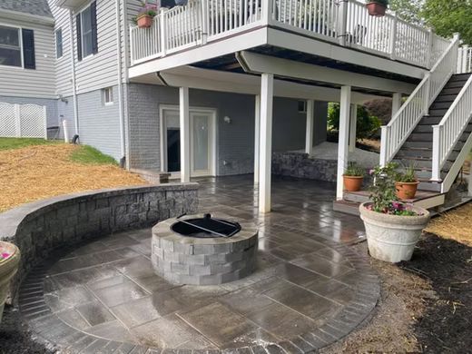Back patio with curved stone fire pit, wet concrete patio, and stairs to an upper deck