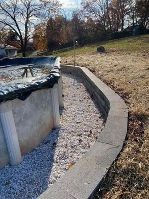 Curved concrete retaining wall edging a gravel garden bed beside dry grass and trees
