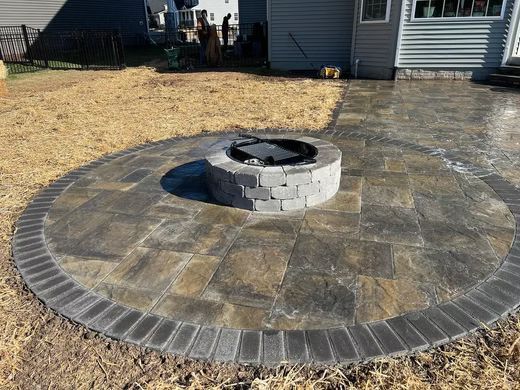 Circular stone patio with a central fire pit in a backyard