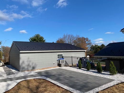 Modern gray garage with paved driveway, fenced patio, and blue sky