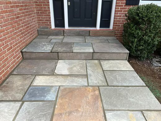 Stone walkway leading to a front door, bordered by brick and shrubs.