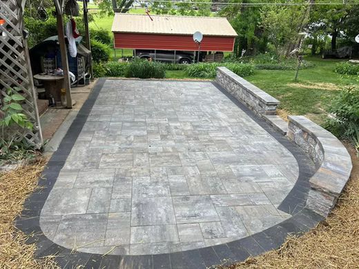 Stone patio with curved steps and dark edging in a backyard garden area