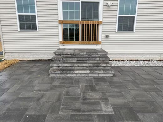 Back patio with stone paver steps leading to a door between two windows, in front of a house