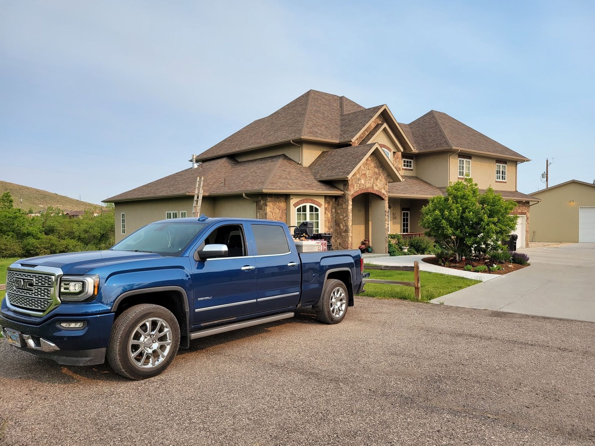 Blue pickup truck parked in front of a large suburban house with a driveway and garage