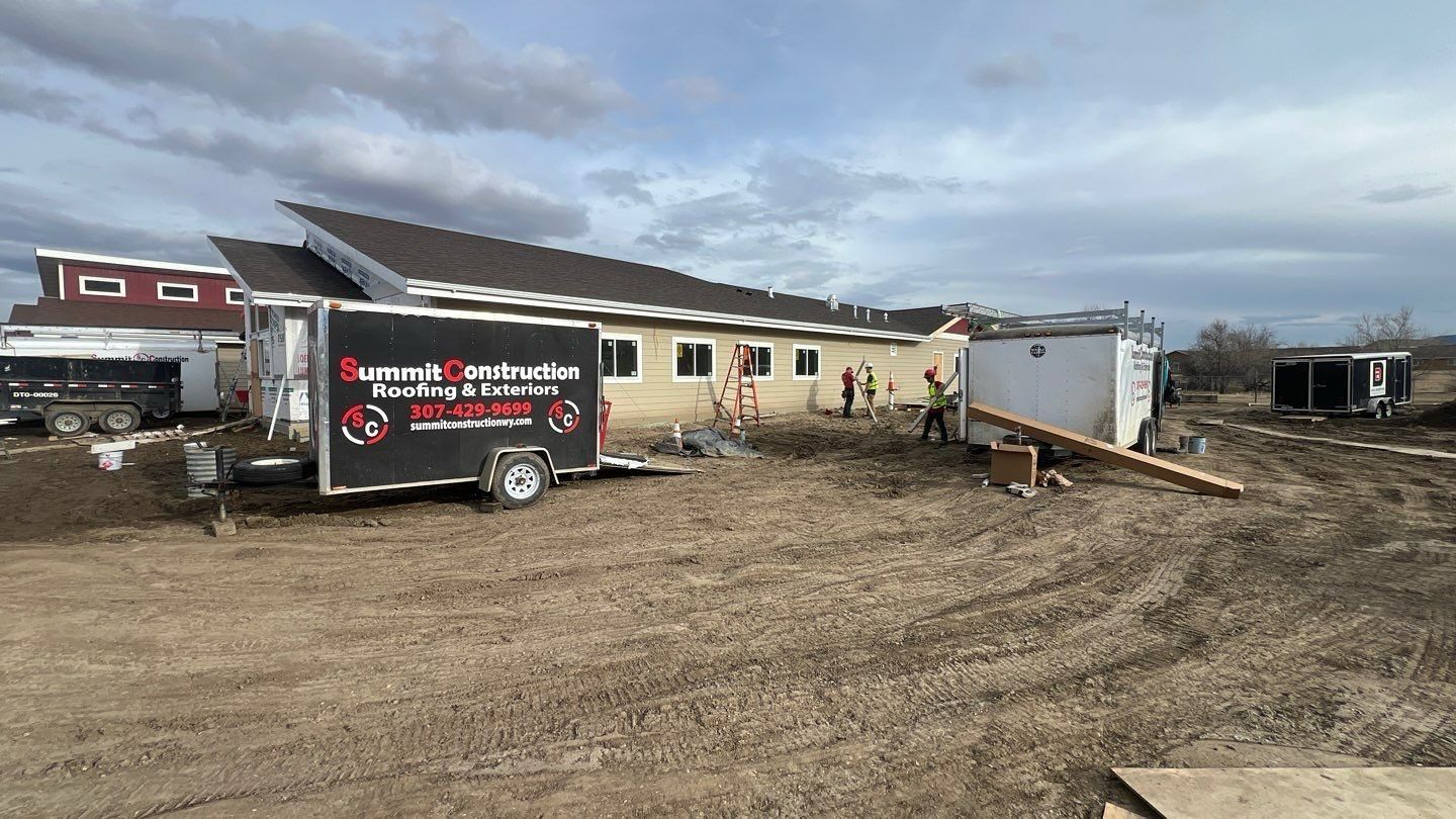 Construction trailer and a beige building on a muddy lot under a cloudy sky