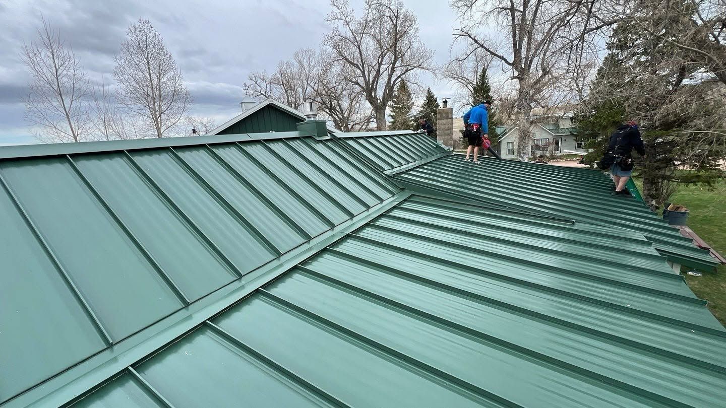 Workers on a green metal roof, inspecting or repairing it on a cloudy day.