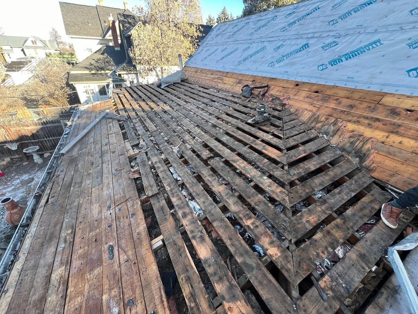 Damaged roof with exposed wooden slats and blue underlayment during repair work