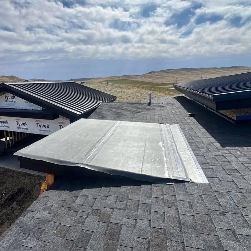 Rooftop with solar panels and a white skylight cover beneath a cloudy sky over open hills.