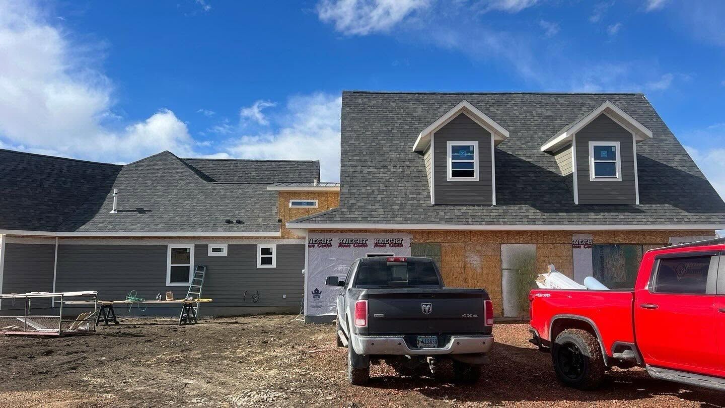 Suburban house with a gray pickup and red truck parked in the driveway under a blue sky