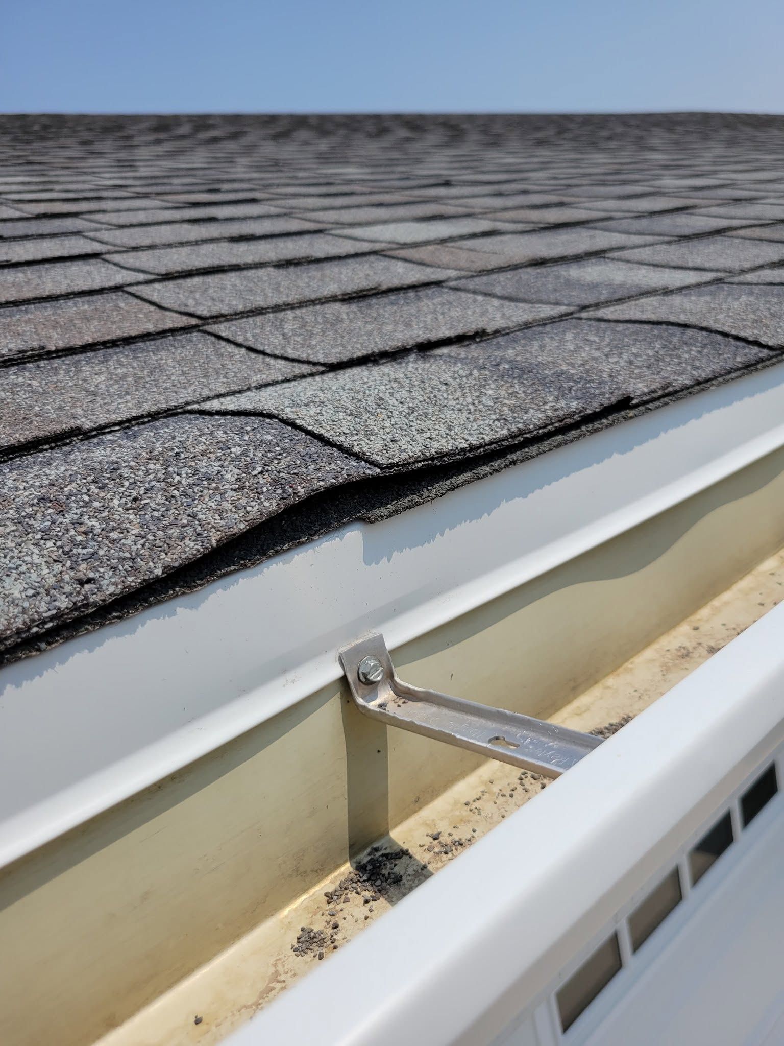 Close-up of a shingled roof edge with gutter and downspout under cloudy sky