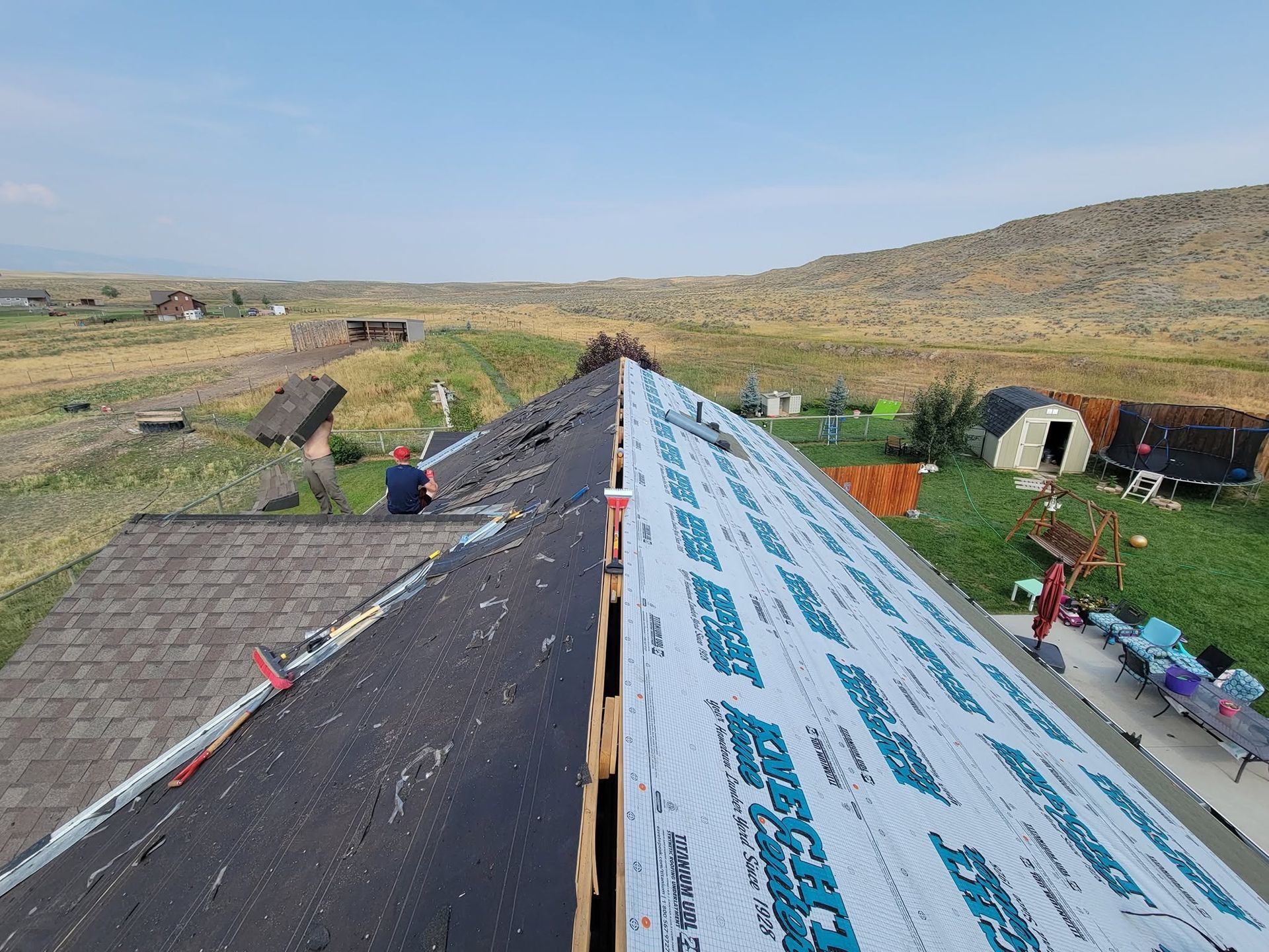 Roof under construction on a rural hillside, with underlayment partly installed and materials nearby