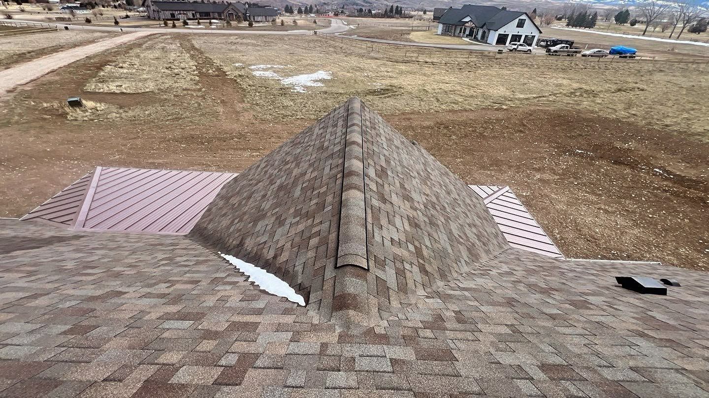 Roof with a central stone chimney vent overlooking a bare suburban lot and distant houses.