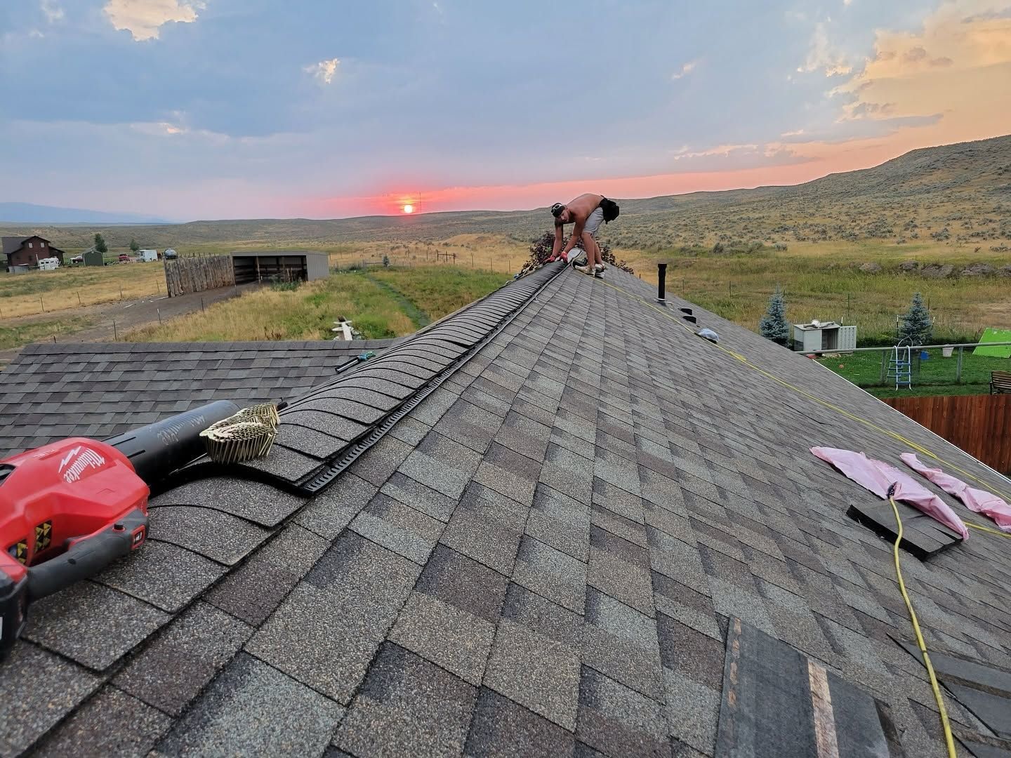Rooftop at sunset with workers near the ridge, overlooking a grassy rural landscape