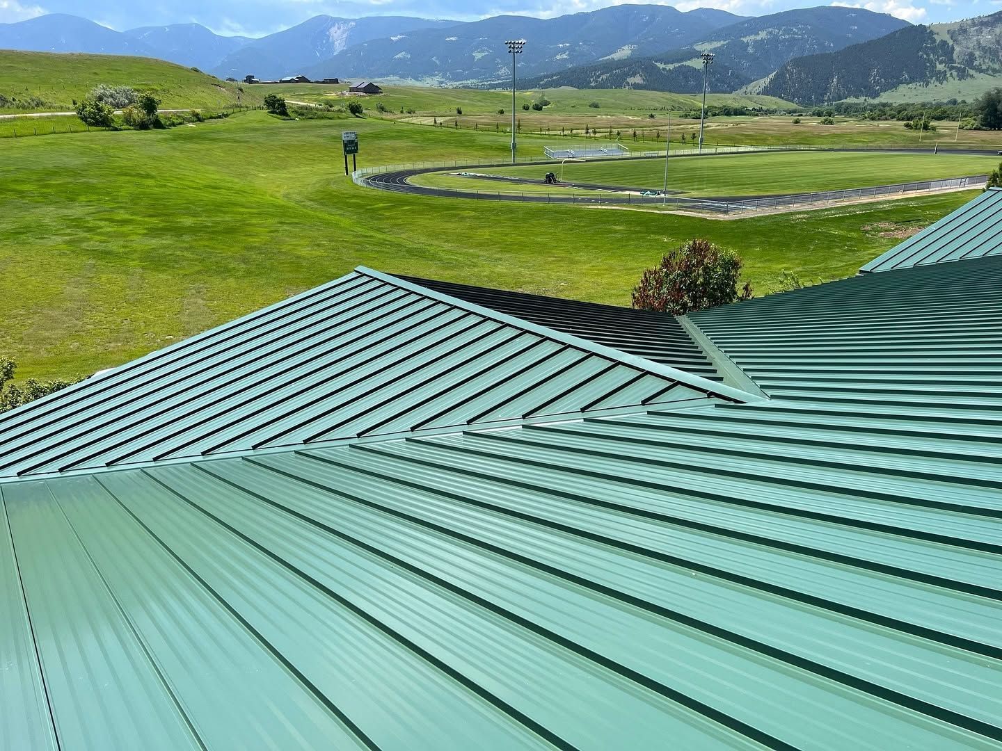 Green metal roof in foreground overlooking a grassy valley and distant mountains under a blue sky