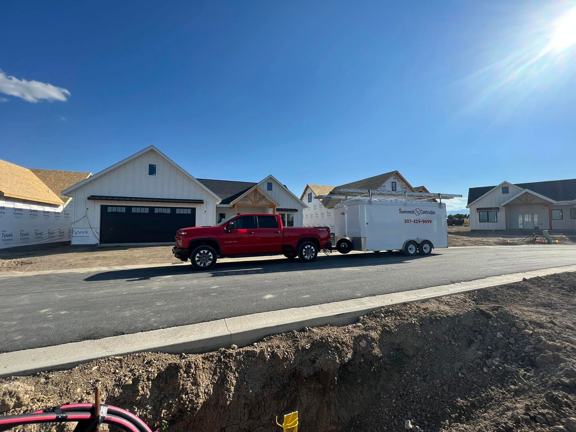 Red pickup truck parked beside a white enclosed trailer on a suburban street under a bright blue sky.