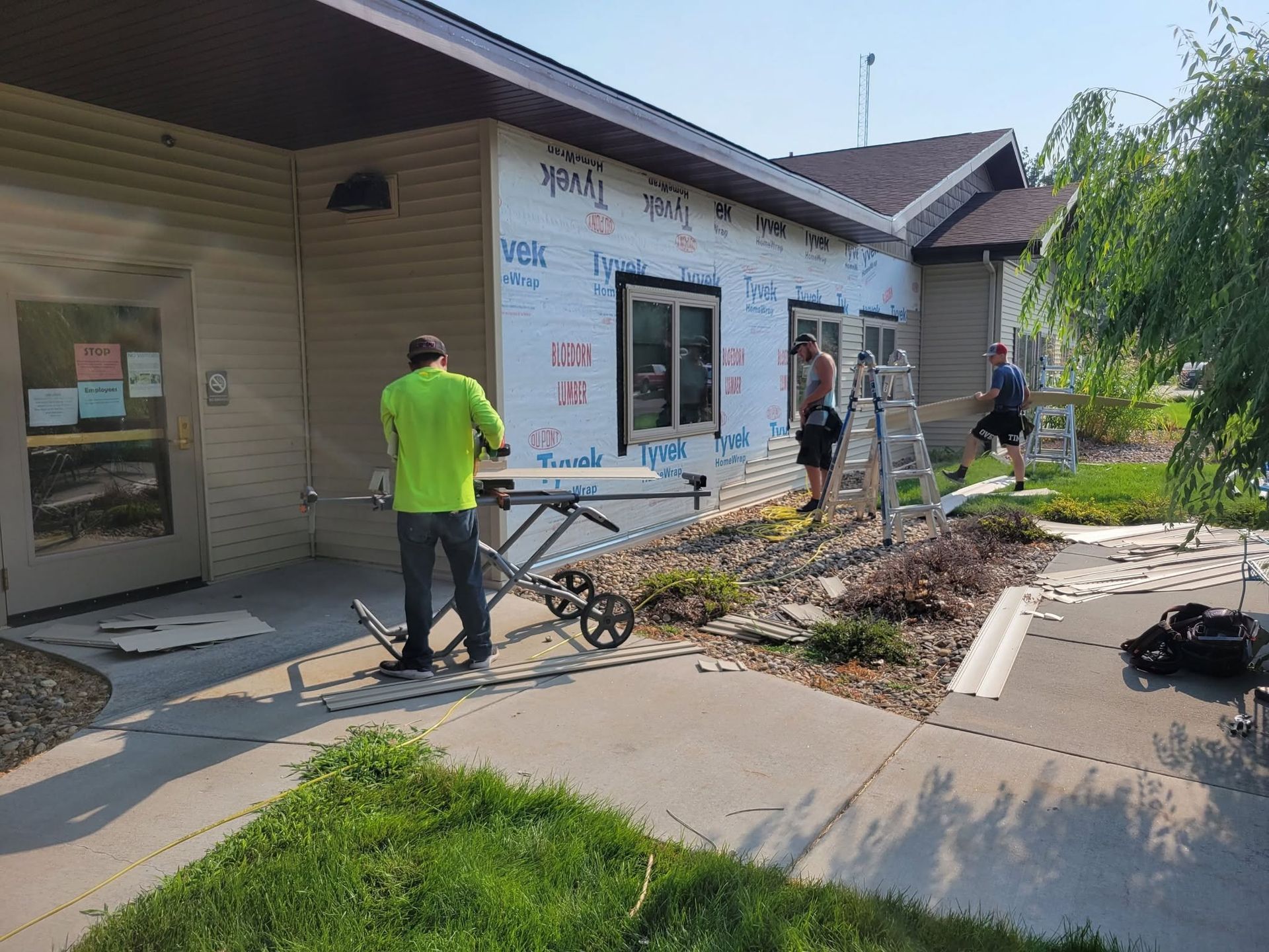 Workers clearing debris outside a white building with a wheelbarrow and tools