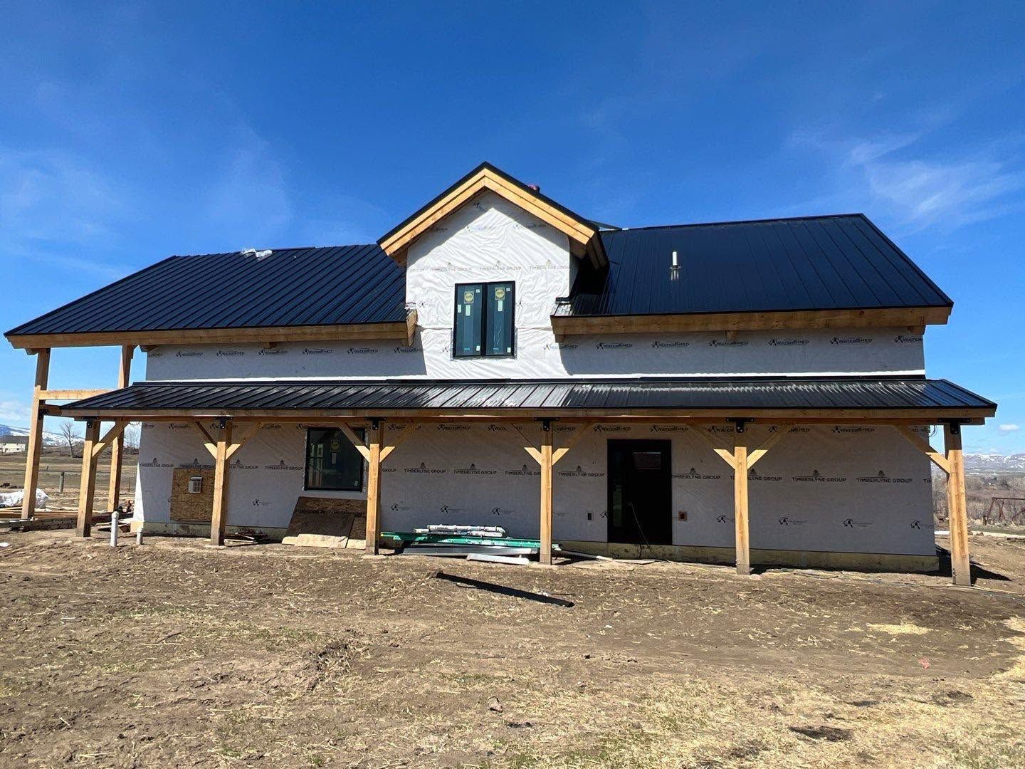 New house with dark roof and wood porch on a bare lot under a blue sky