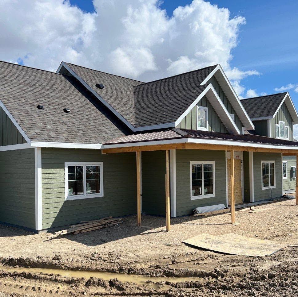 New house exterior with green siding, gray roof, and a covered front porch under construction.