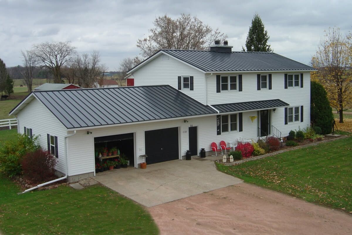 White two-story suburban house with gray metal roof, attached garage, and a driveway in a grassy yard