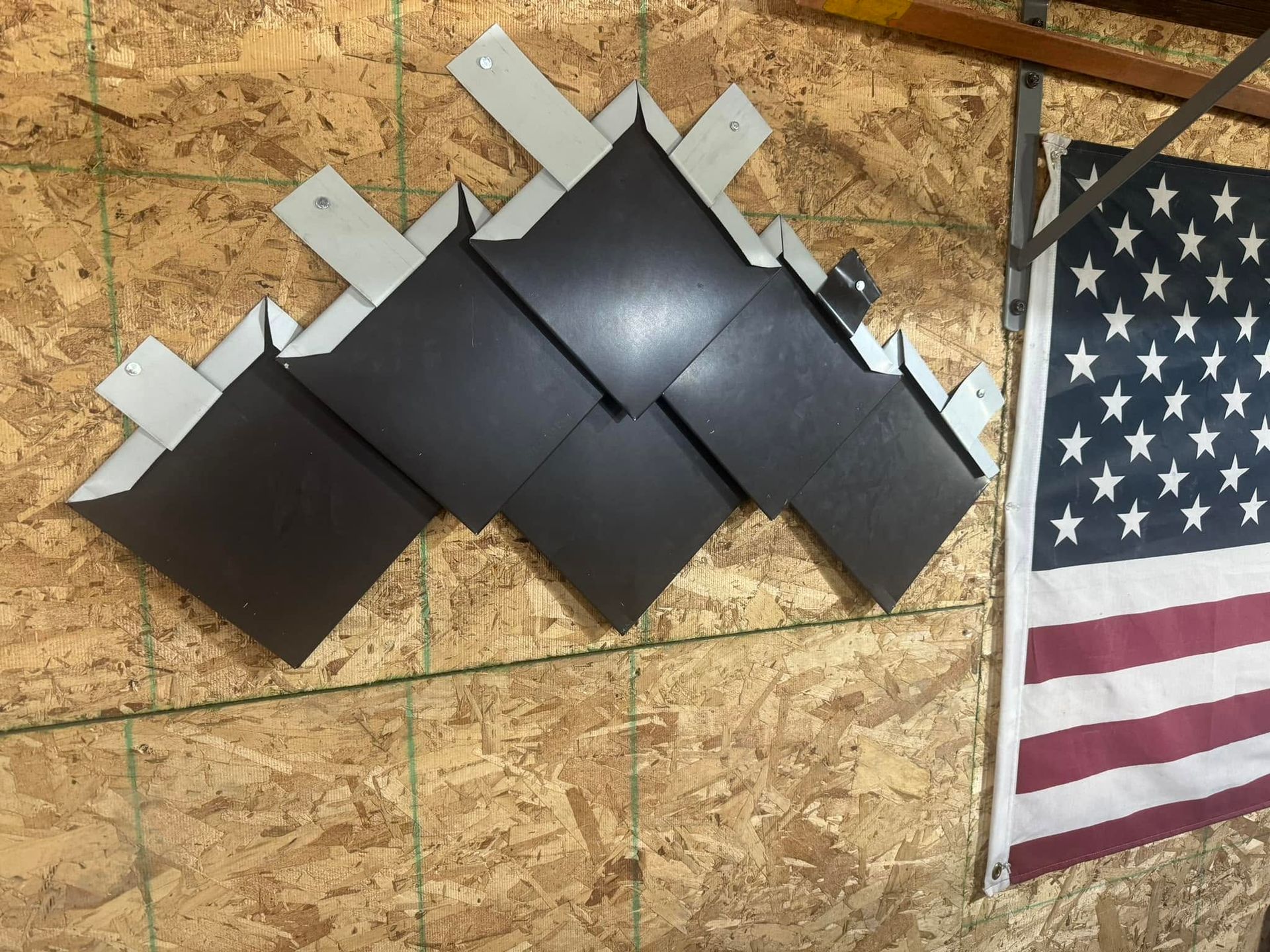 Black geometric wall art with silver accents mounted on plywood beside an American flag