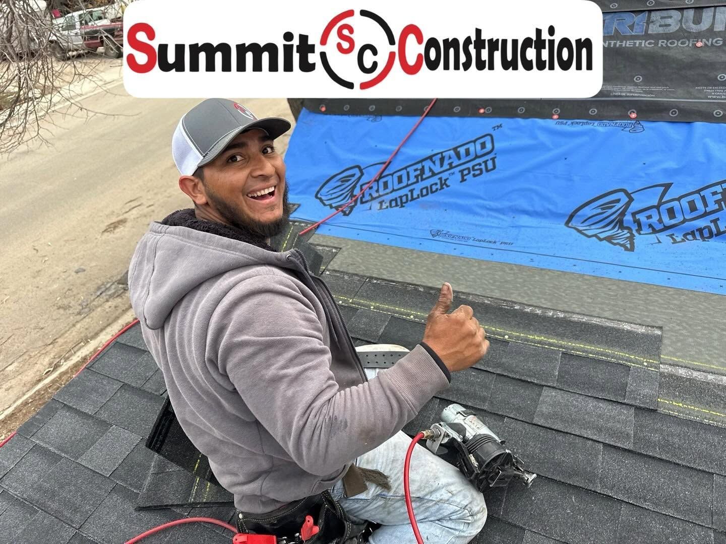 Worker kneeling on a roof, smiling and giving thumbs up beside Summit Construction logo