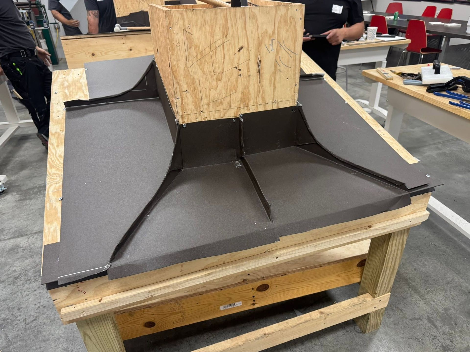 Black foam ramp prototype on a wooden workbench in a workshop with a plywood backing panel