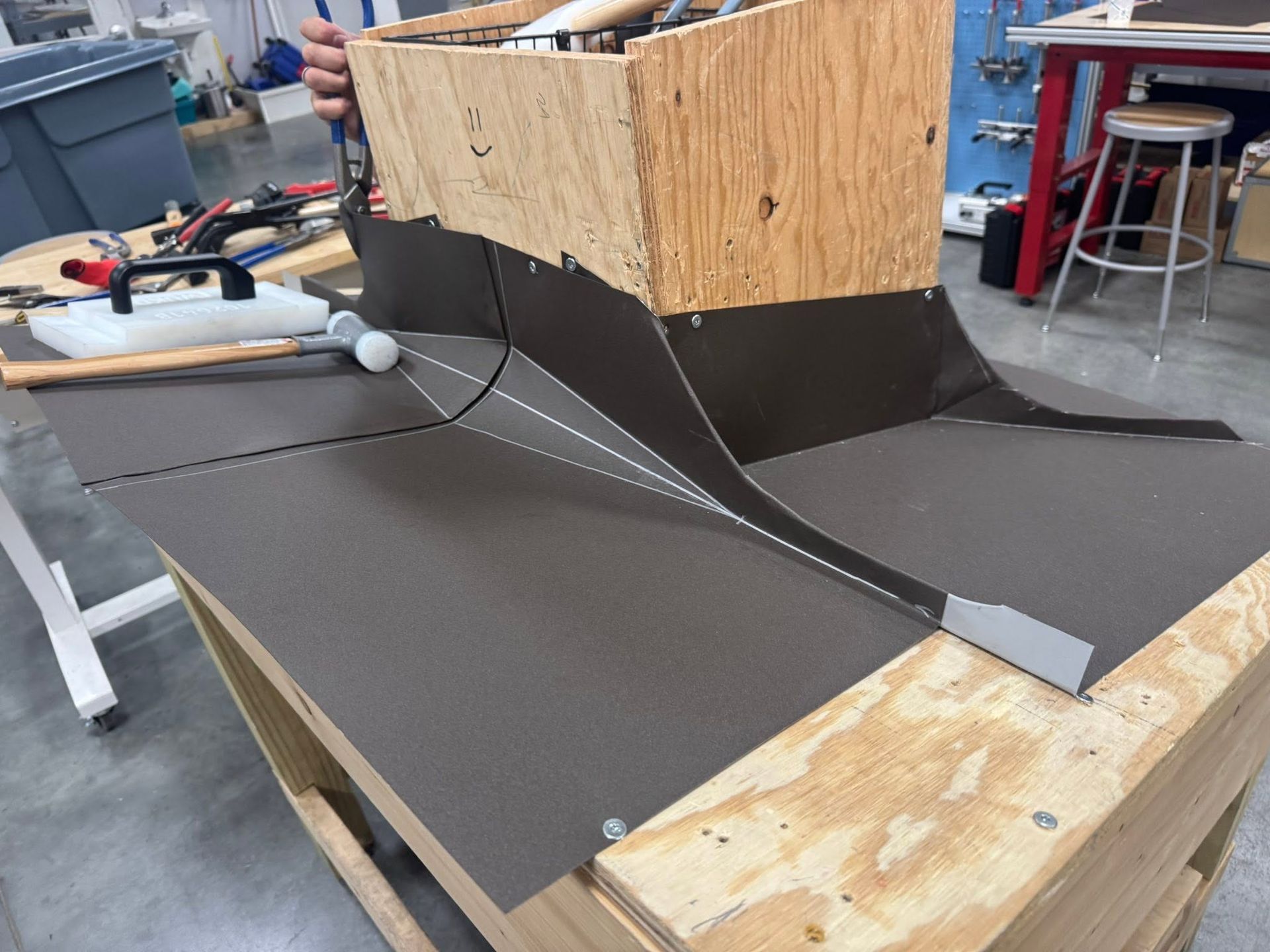 Workshop table with a wooden ramp prototype covered in dark material and a sloped channel structure