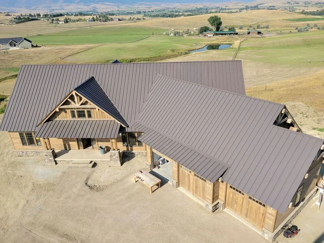 Aerial view of a large dark gray roofed house in a rural field with surrounding open land.