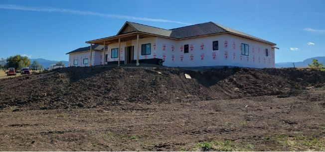 Single-story house under construction on a dirt hillside under a clear blue sky