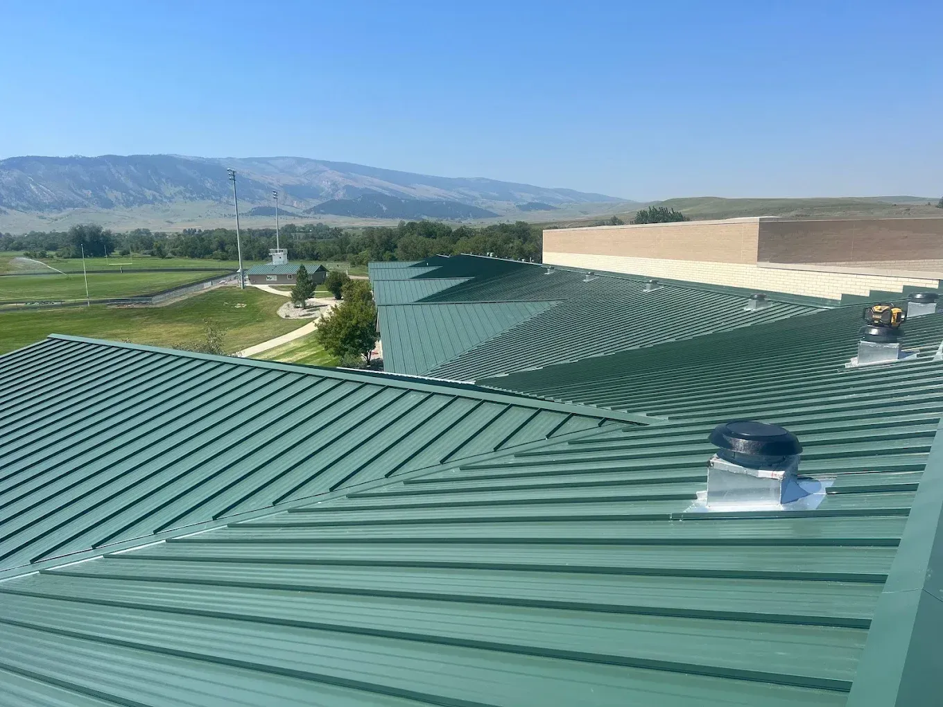 Green metal roof with vents overlooking hills and a valley under a clear sky