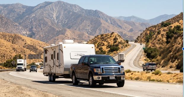 Pickup truck towing a white RV on a desert highway with mountains in the background