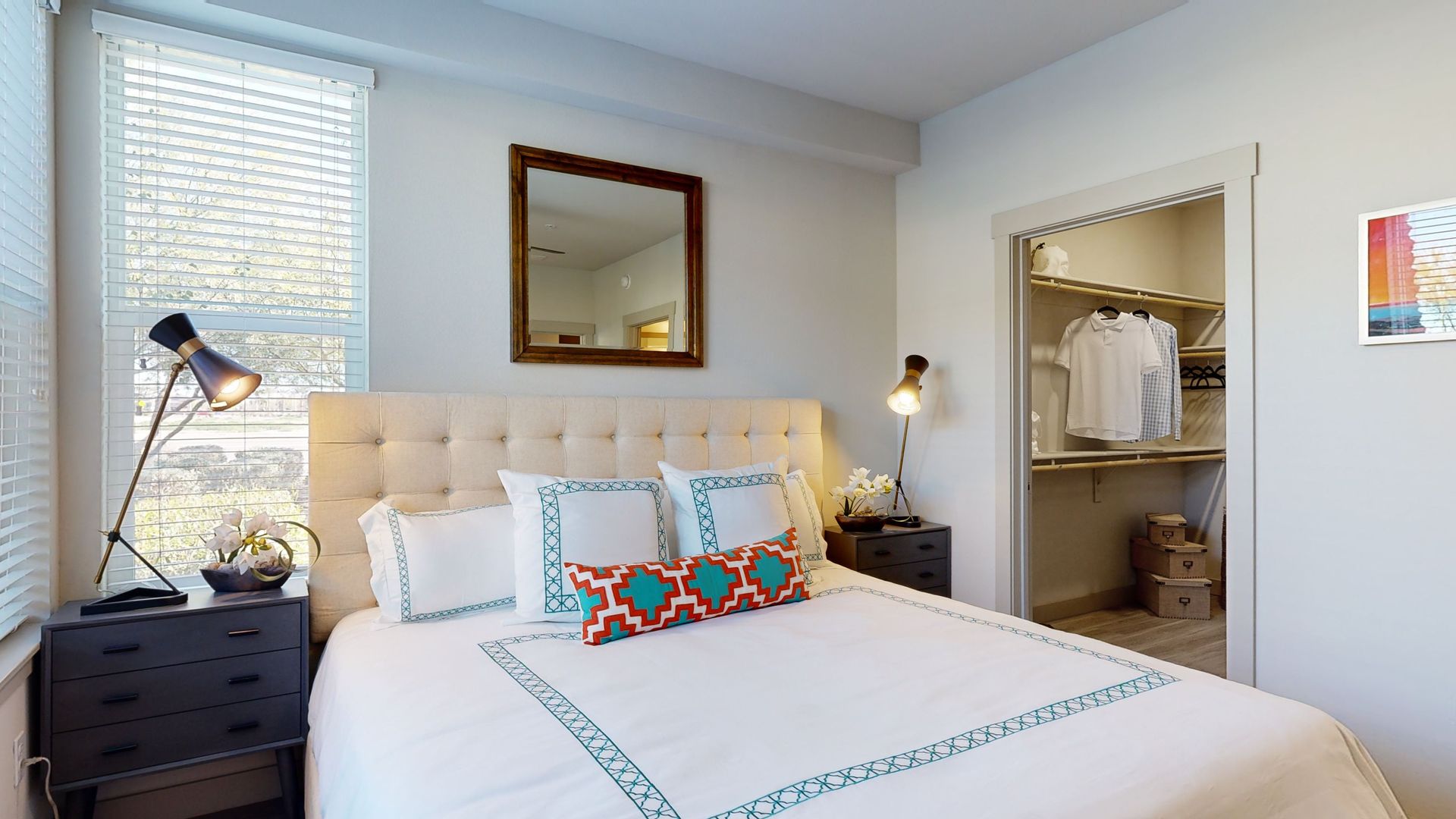 A bedroom with a bed , nightstand , lamp , mirror and walk in closet.