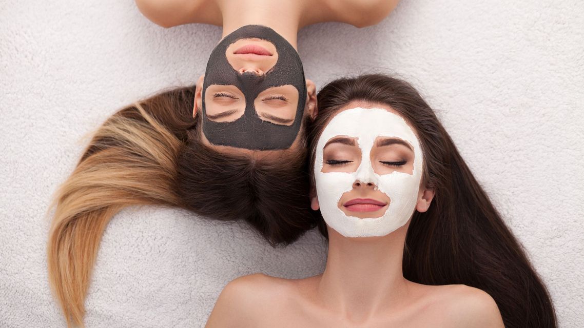 Two people with face masks relaxing on a white surface, one with a black mask and one with a white mask.