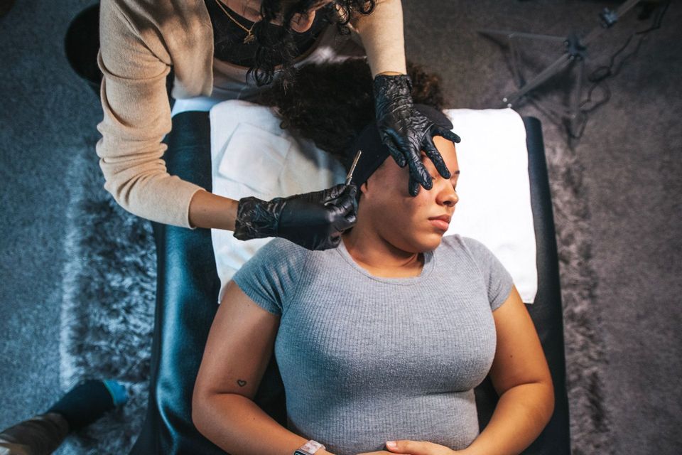 Person receiving a cosmetic procedure on the side of their face. A gloved person works over them.
