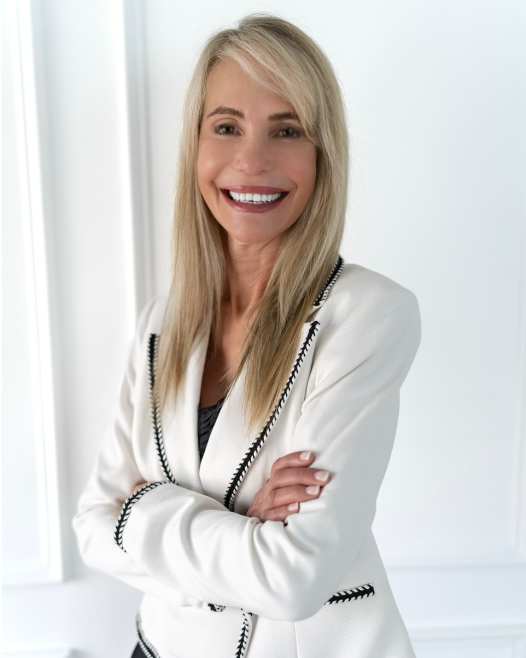 A woman in a green jacket is smiling with her arms crossed.
