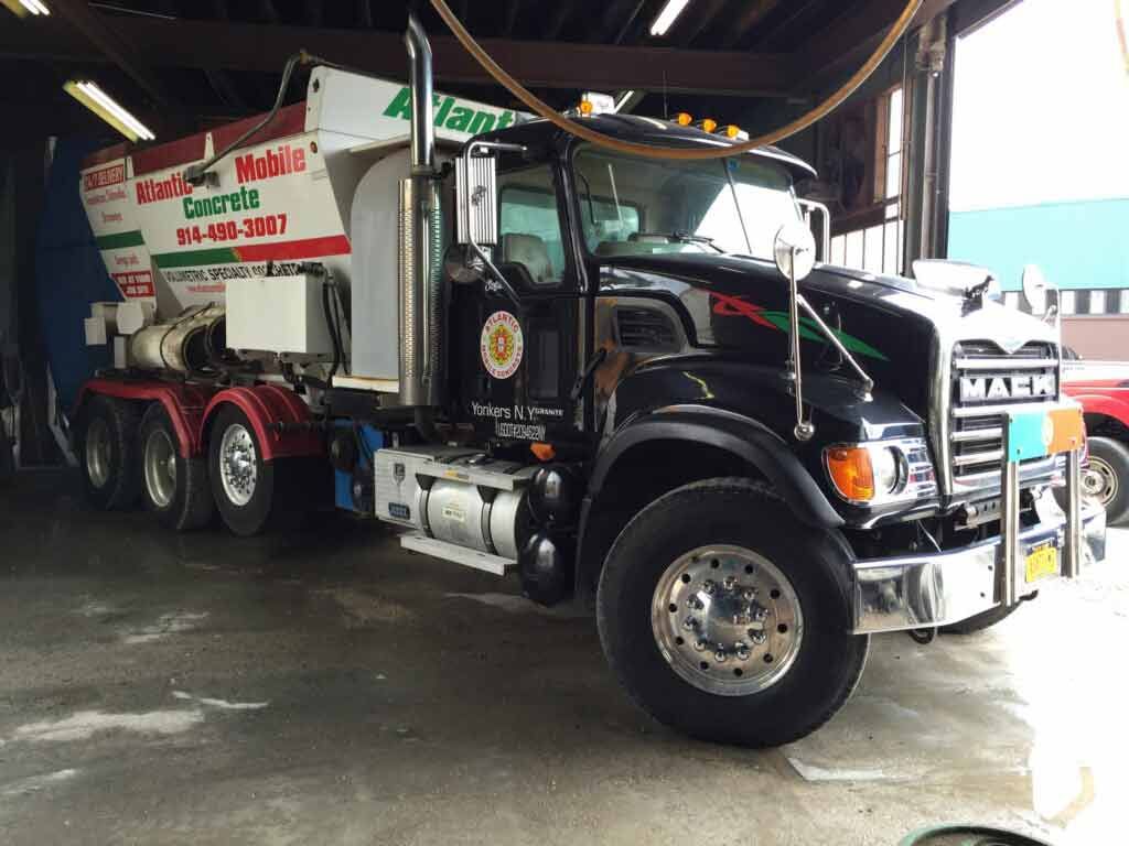 Black dump truck parked inside a covered garage, with red and white equipment on the back.