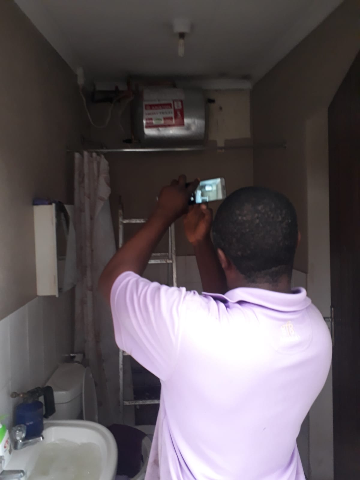 Plumber electrician taking a photo of a wall mounted geyser installation
