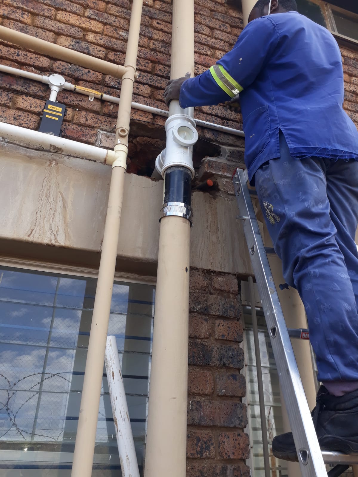 worker standing on a ladder installing external wall mounted sewage plumbing pipes