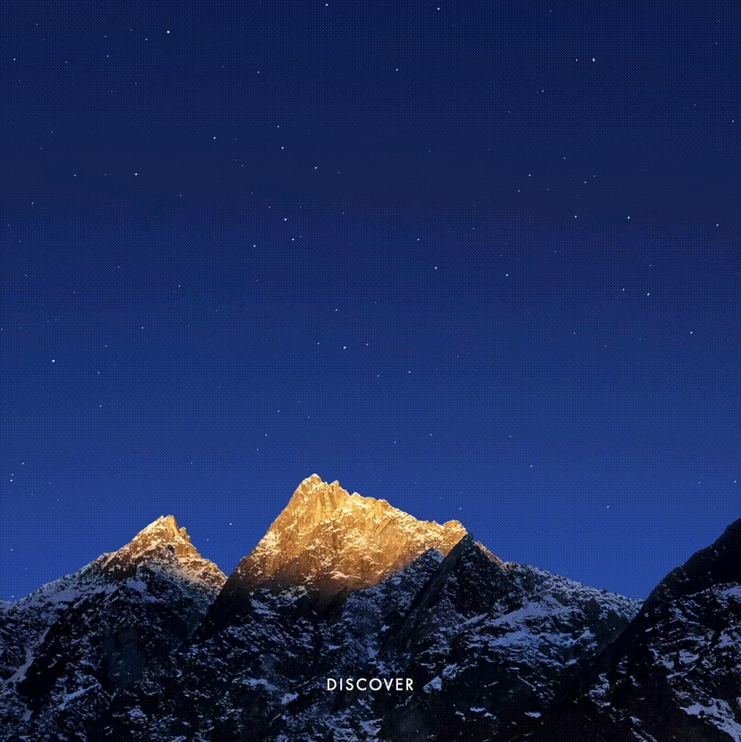 Snow-capped mountains illuminated by golden light under a dark blue, starry night sky.