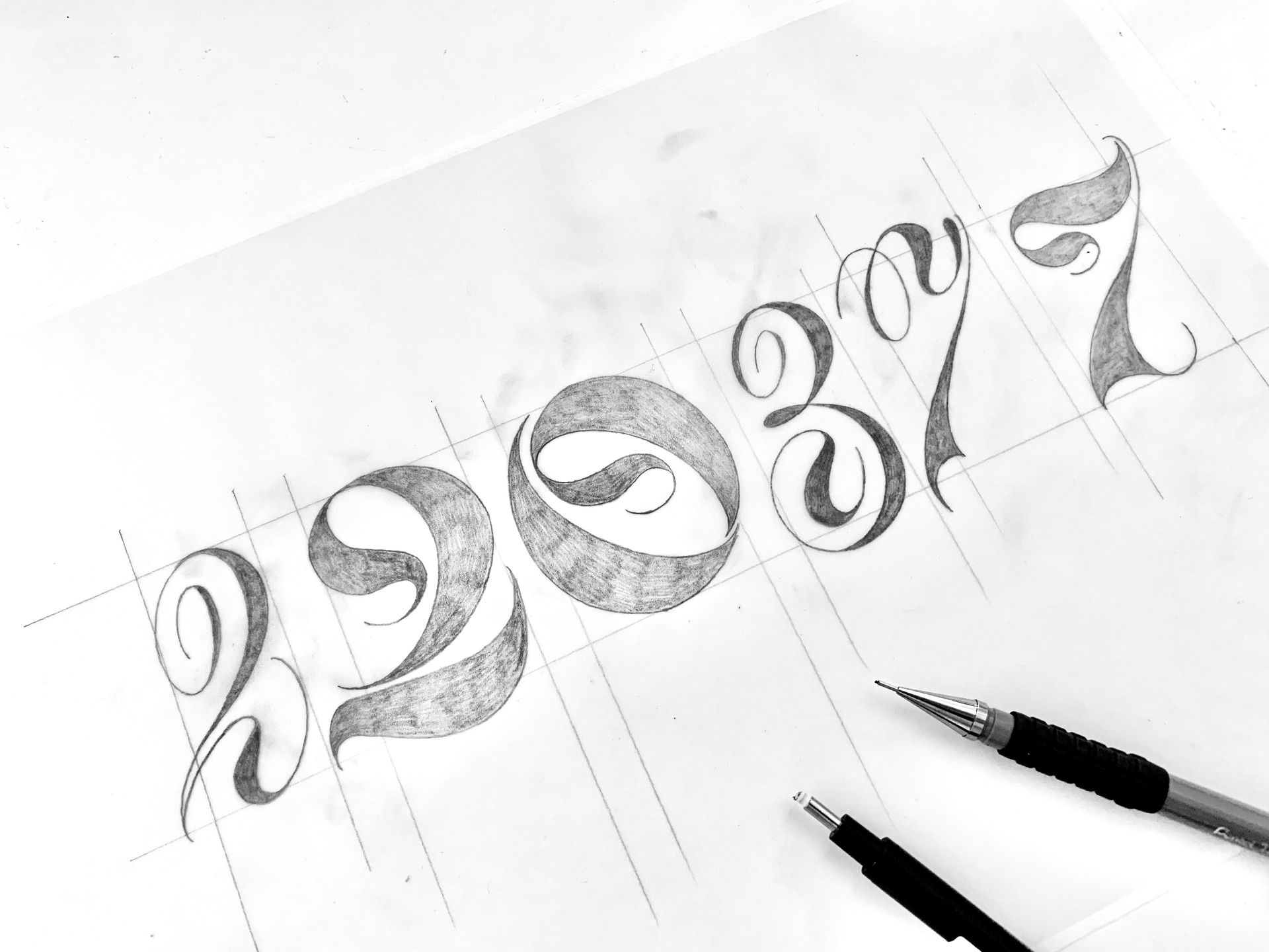 Pencil sketches of stylized numbers on paper with drawing pens beside them