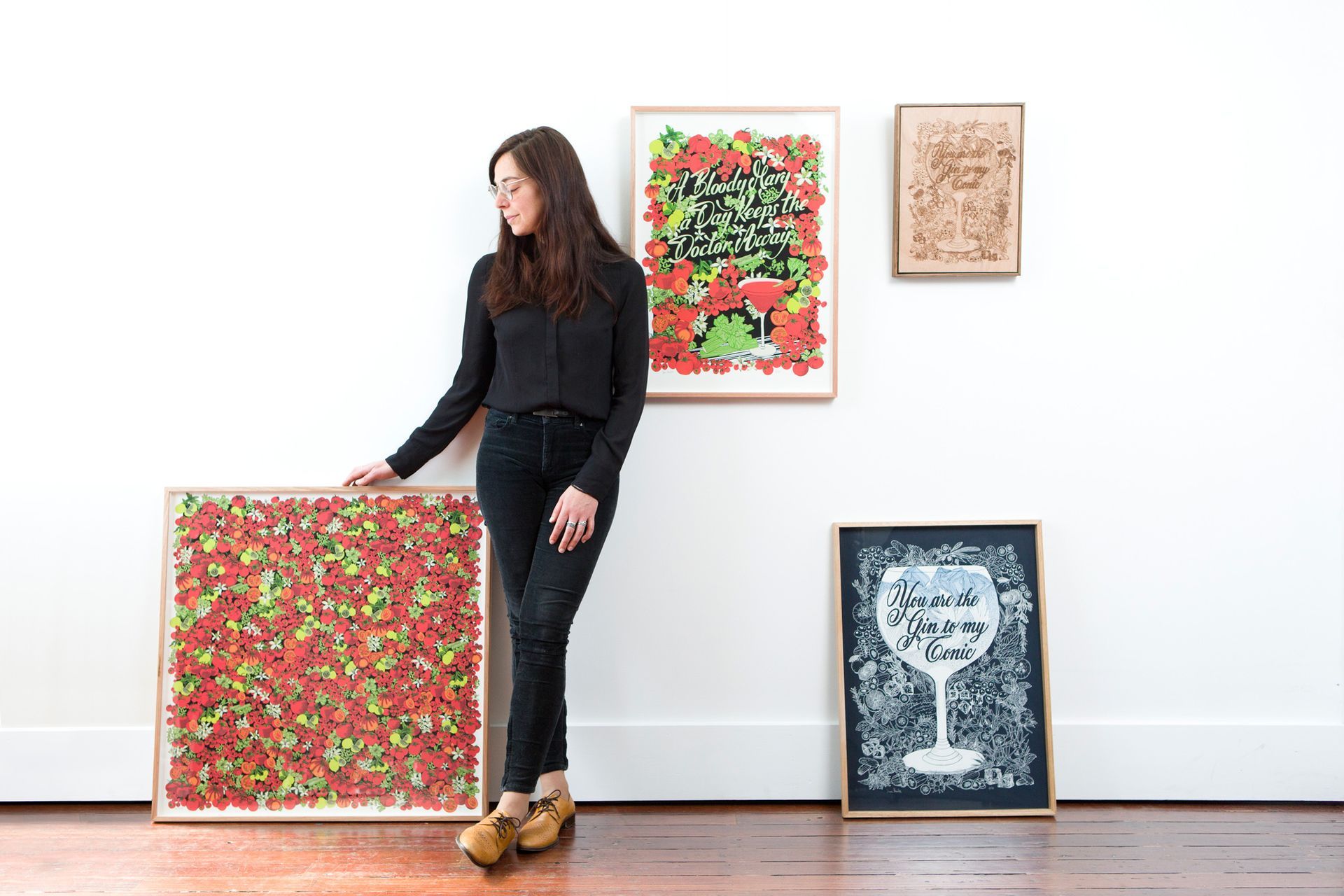 Maria Montes standing beside colorful framed artwork displayed on a white gallery wall