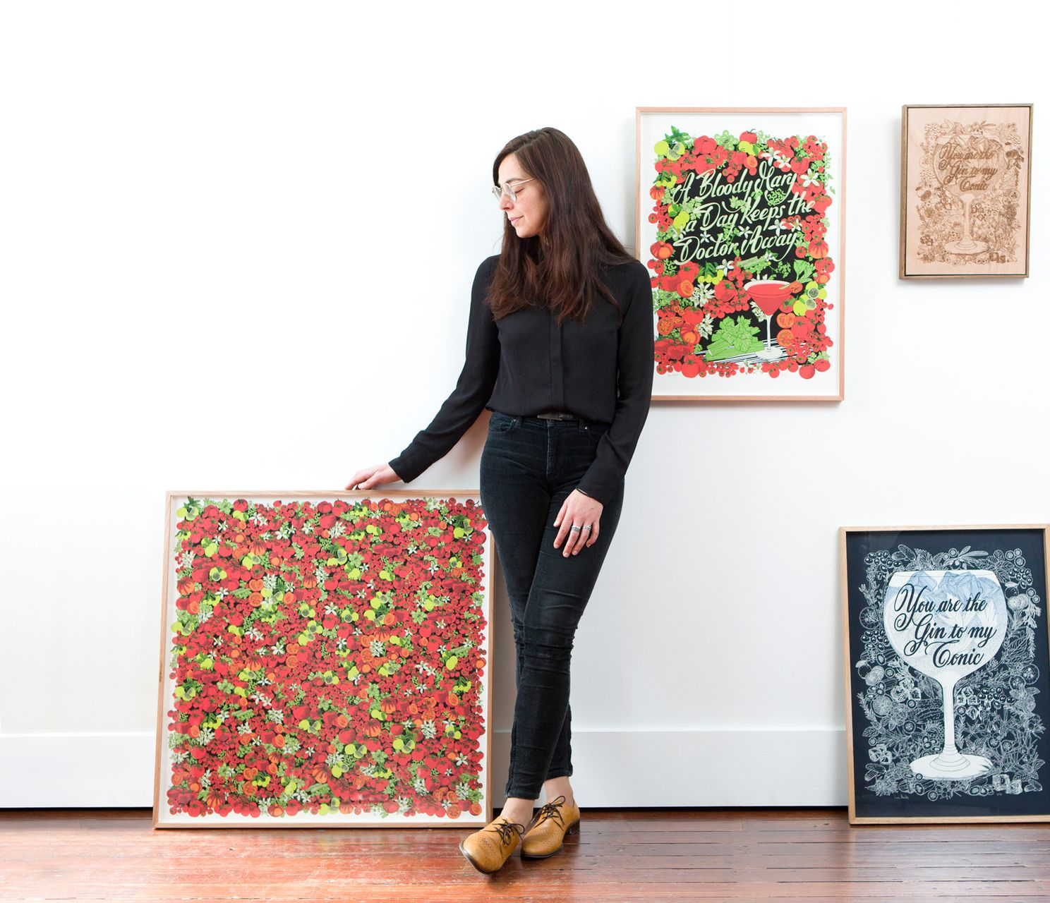 Maria Montes in black stands beside colorful floral artwork in a white gallery-style room.