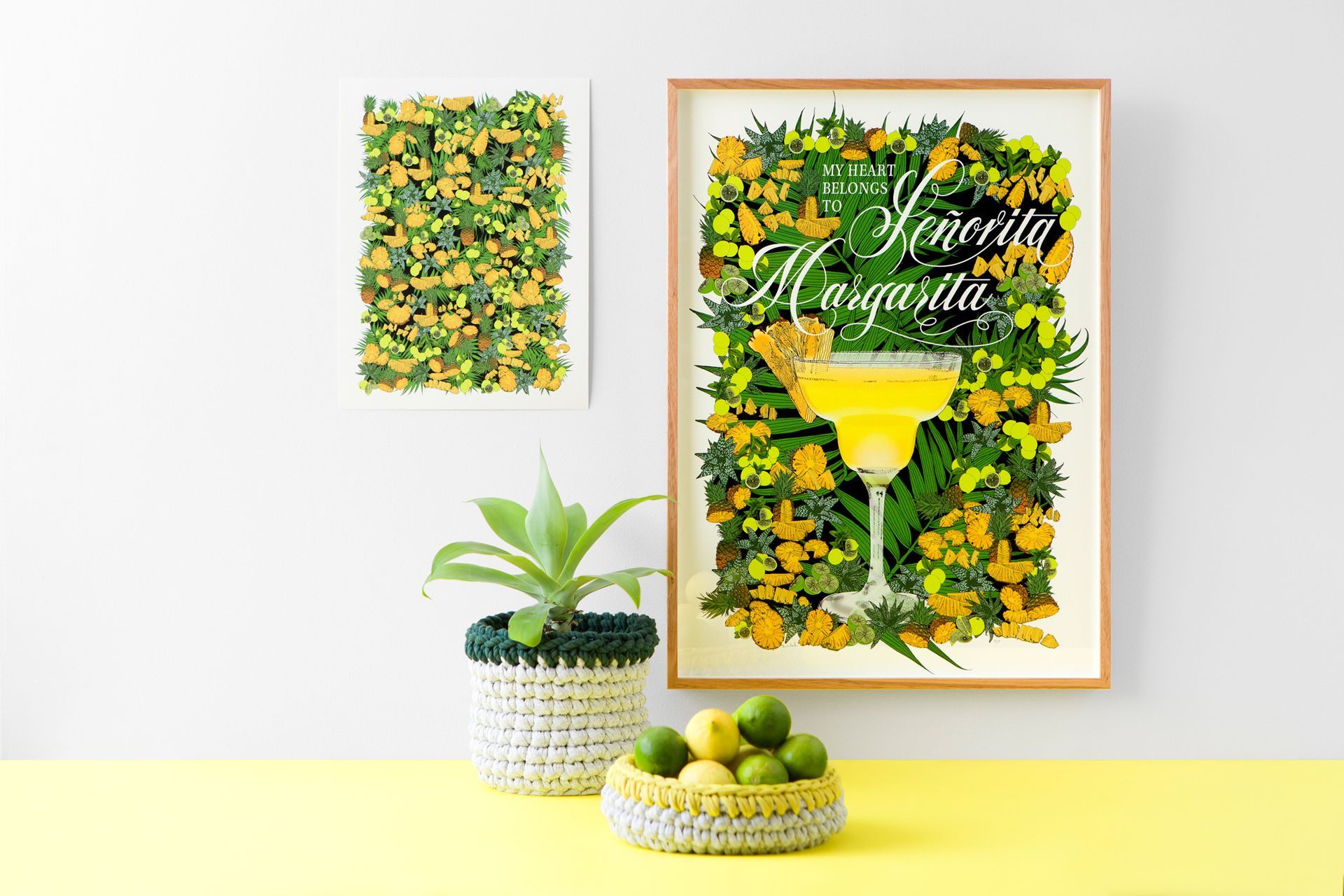 Stylized yellow-green floral wall art above a plant and bowl of limes on a white shelf