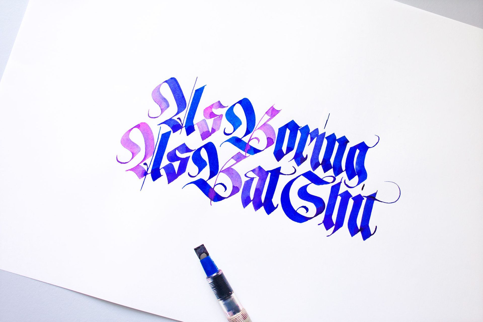 Gothic calligraphy in blue and purple ink on white paper, reading