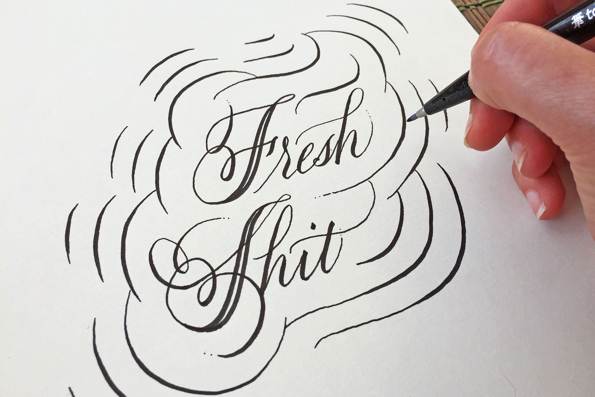 A hand uses a pen to ink elegant black calligraphy that reads