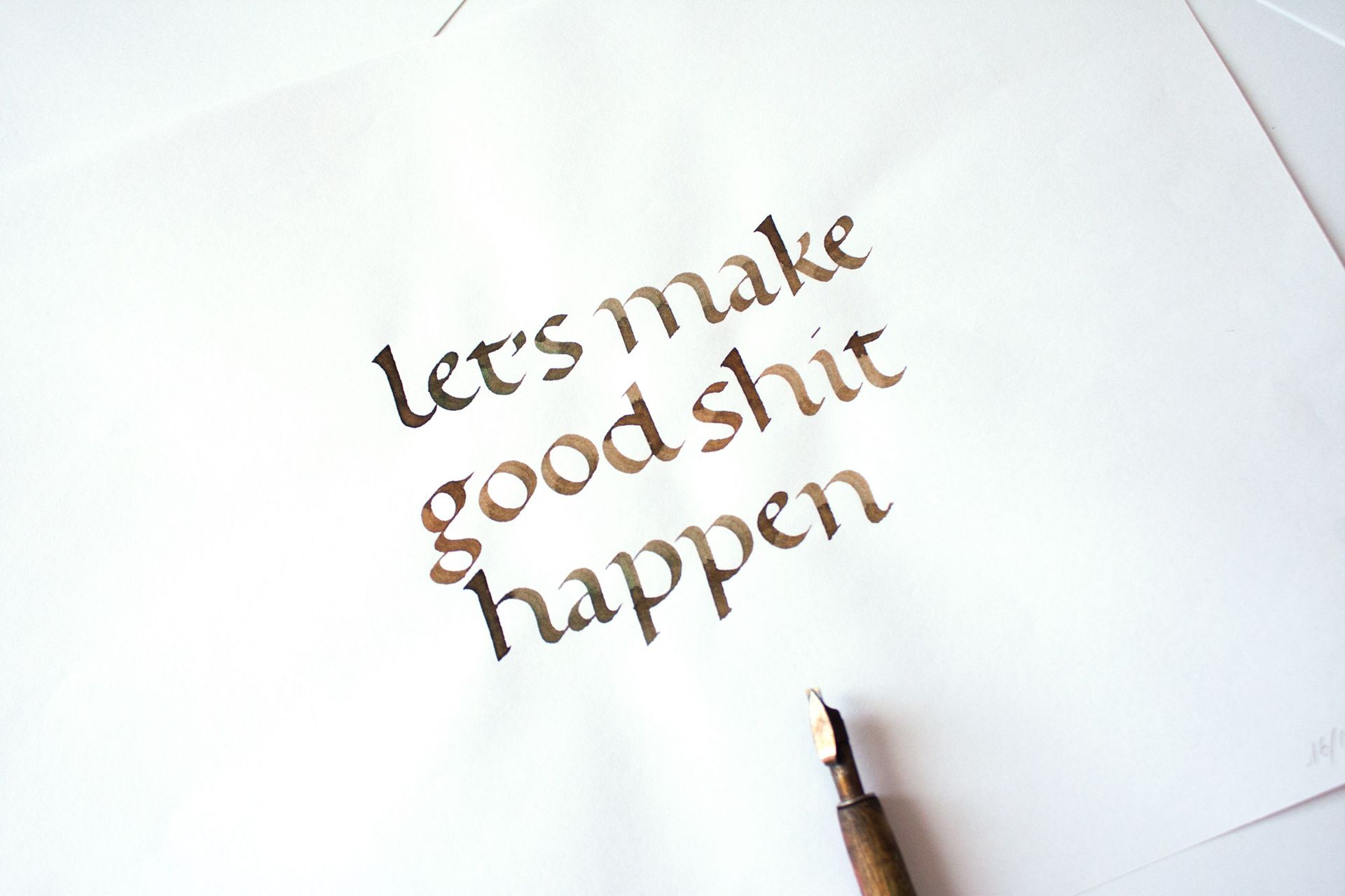 A fountain pen rests on white paper featuring the hand-lettered dark brown text: