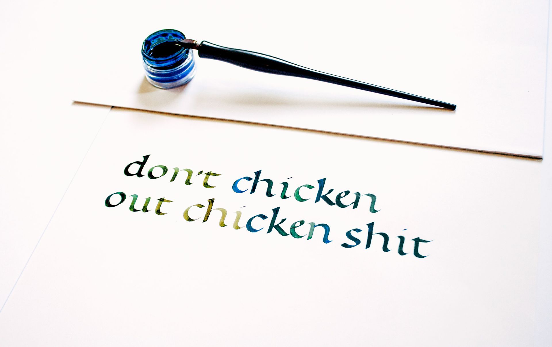Calligraphy written in blue ink on white paper reads,