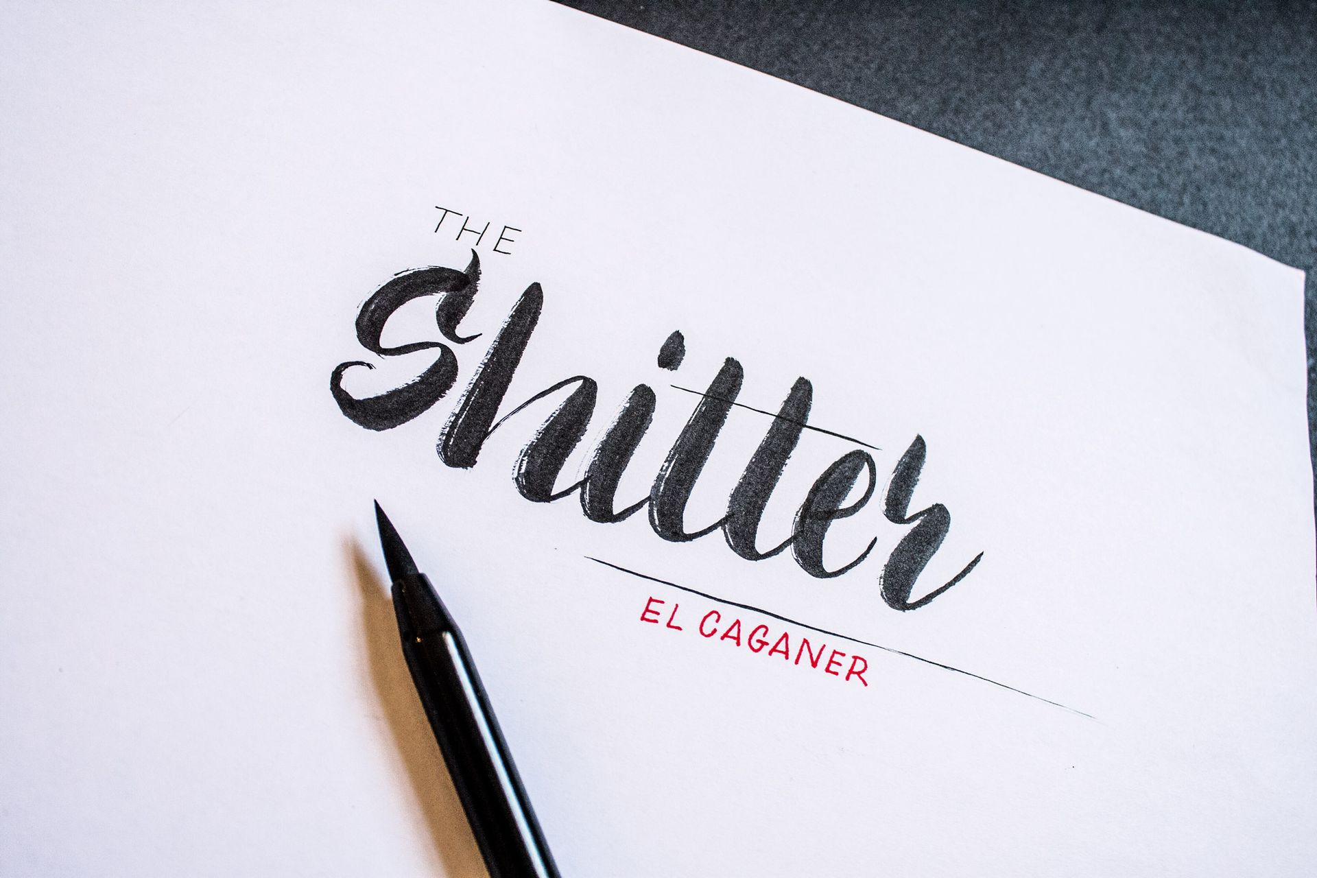 A black calligraphy pen lies on white paper inscribed with 