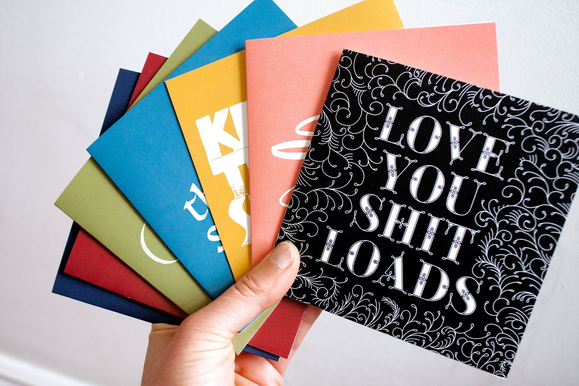 A hand fans out colorful greeting cards, the top one reading 