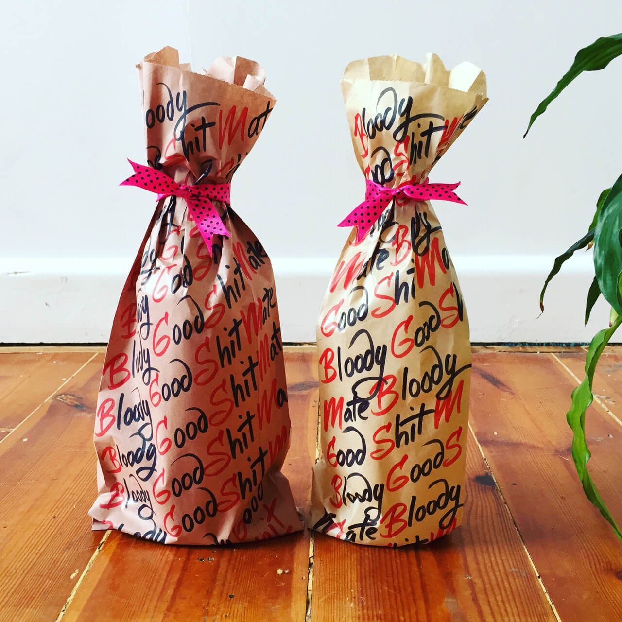 Two brown paper gift bags tied with pink ribbons, printed with black and red 